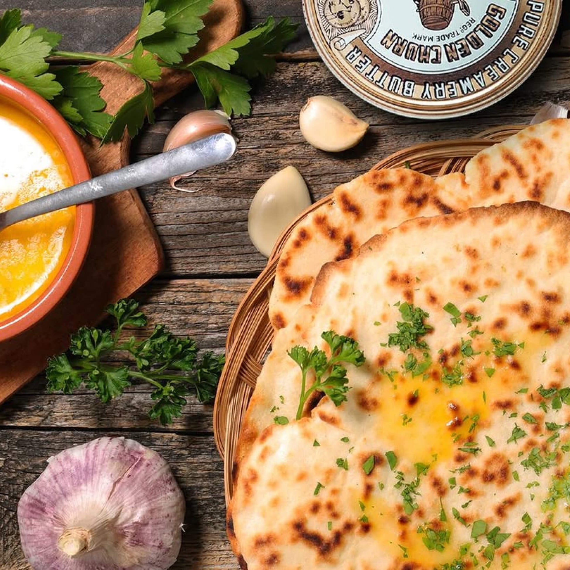 Flatbread with herbs on a wooden table with a tin of Golden Churn Butter